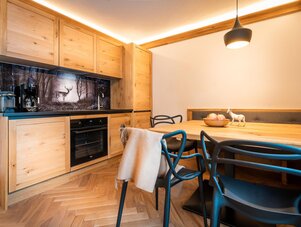Wooden kitchen with cabinets, black countertop, oven, and dining table.