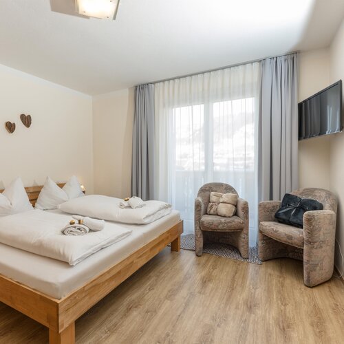 Wooden bed with white bedding and two armchairs by window