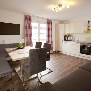 Open-plan living area with dining table, seating, and white kitchen