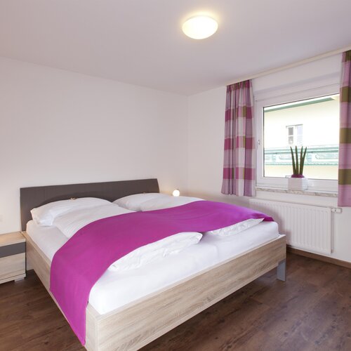 Bedroom with double bed, purple bed runner, striped curtains