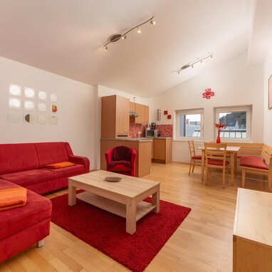 Bright living area with red sofa, dining table, and kitchenette