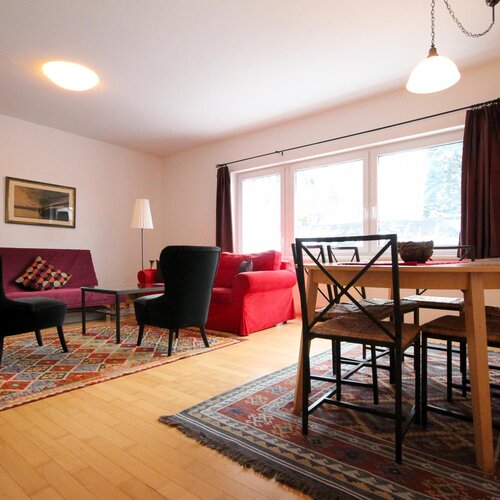 Living room with purple sofa, red chair, and colorful rug. | © SCHLADMING-APPARTEMENTS