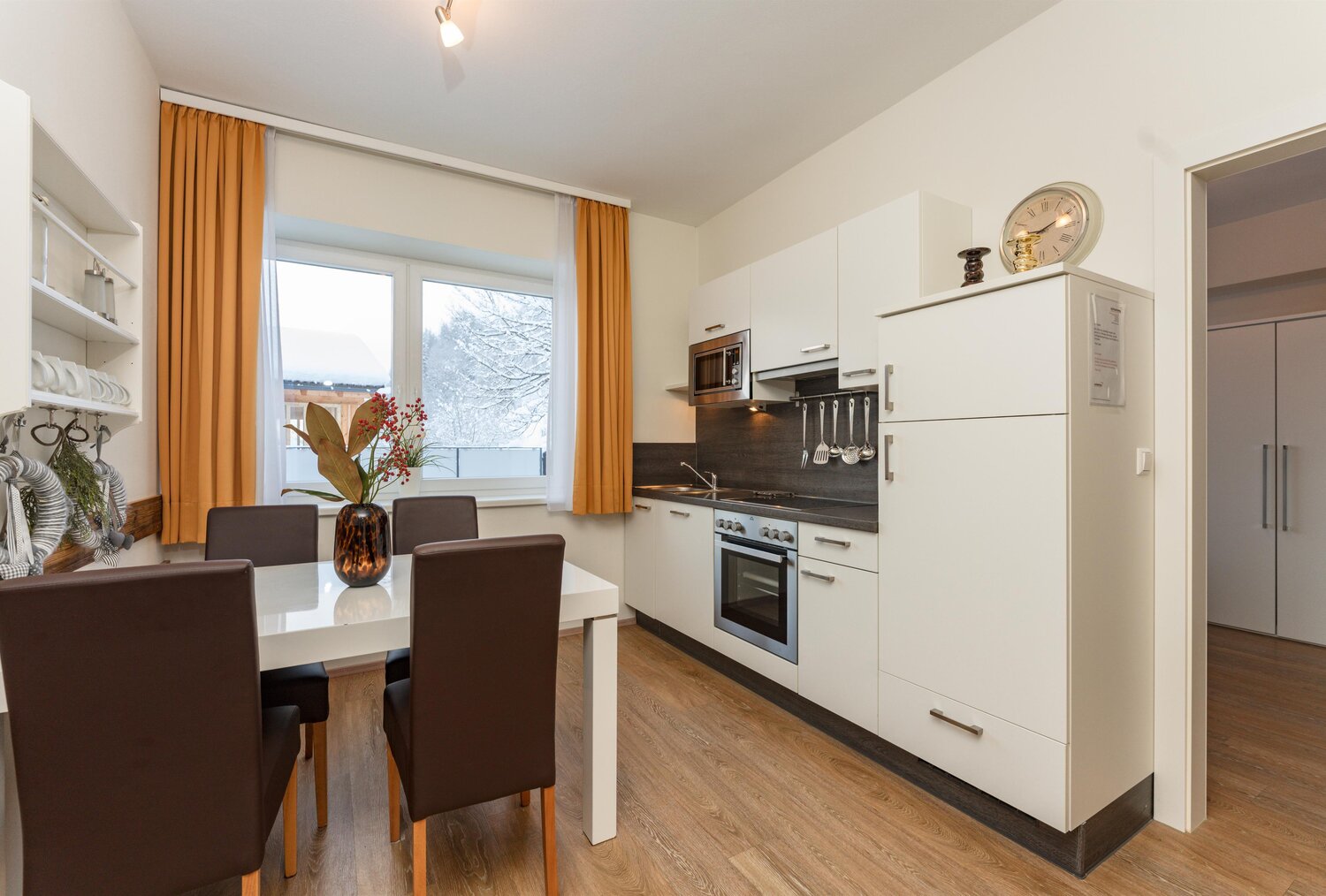 Modern white kitchen with oven, dining table, orange curtains