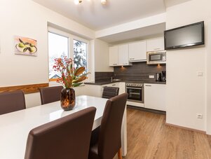 Modern kitchen with white cabinets, dining table, and TV