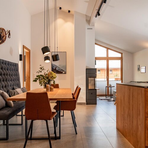 Open-plan dining area with wooden table, tufted bench, and pendant lights.
