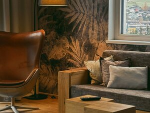 Cozy living room with leaf-pattern wallpaper, leather chair, and wooden cube tables