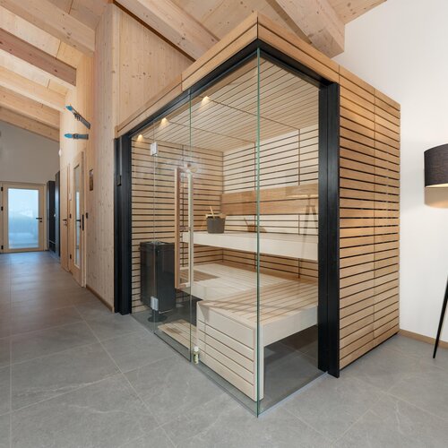 Hallway lined with light wood leading to glass sauna with floor lamp