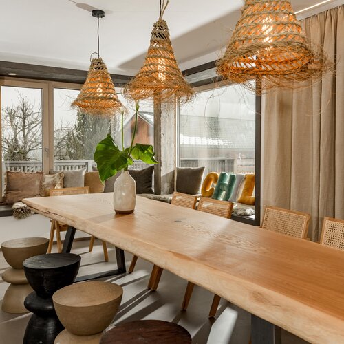 Long wooden dining table under three woven pendant lamps