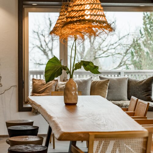 Long wooden dining table with vase and large leaves