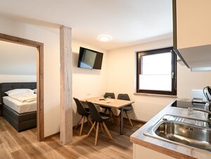Open-plan room with kitchen, dining table, and bedroom doorway.