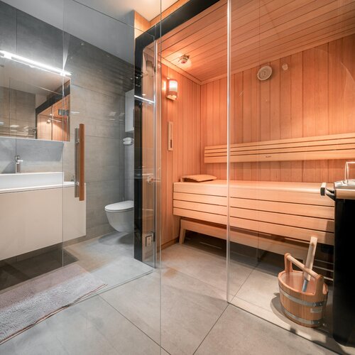 Modern bathroom with glass wall separating shower from wooden sauna.