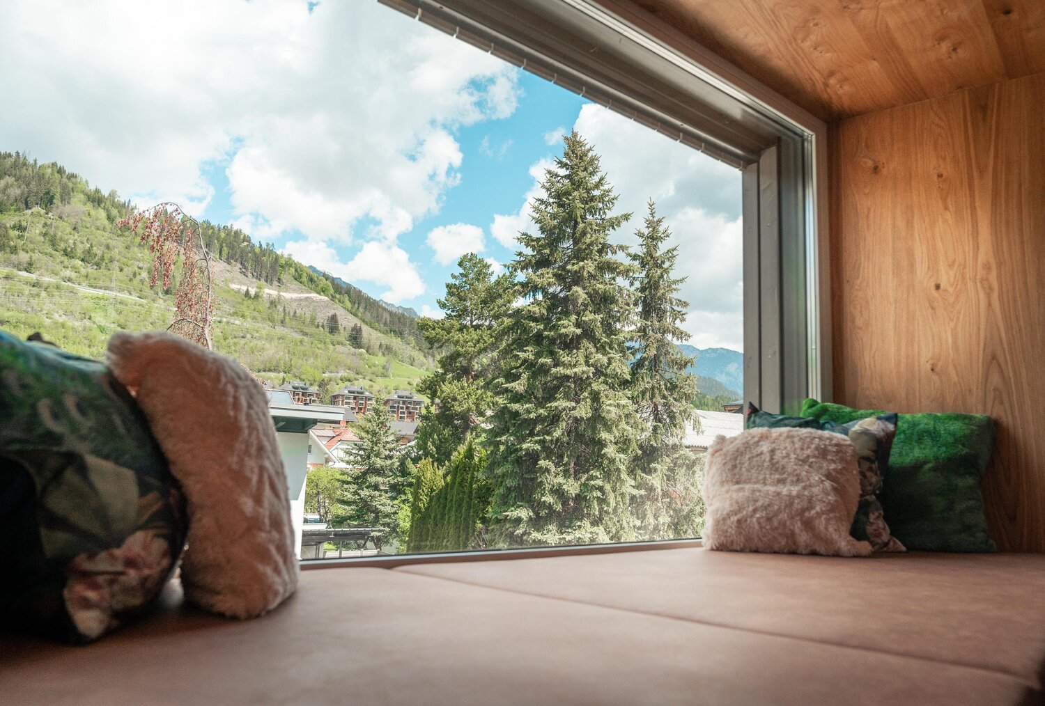 Cozy window seat indoors with mountains and trees outside.