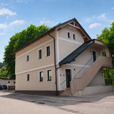 Two-story beige building with an outdoor wooden staircase beside trees