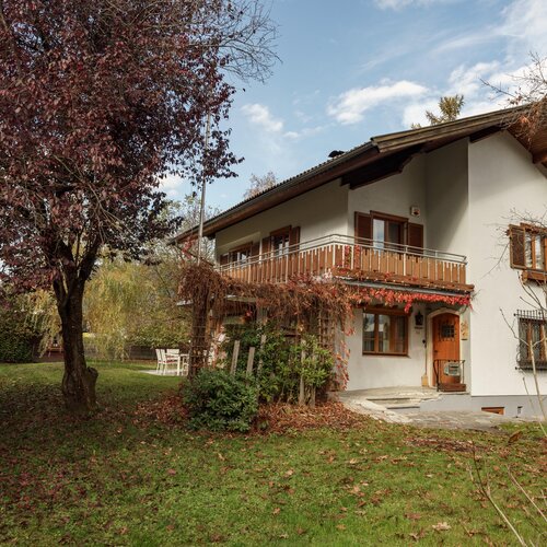 Two-story white house with wooden balcony and autumn garden