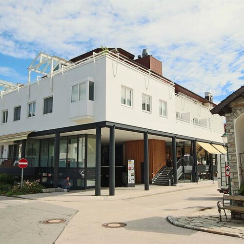Modern white building with glass storefronts and a small stone shrine nearby