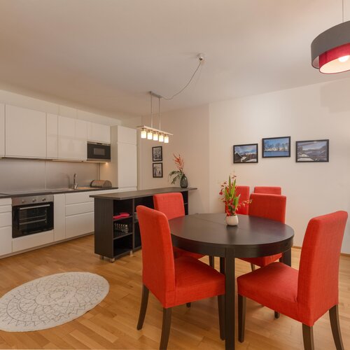 Open-plan kitchen with dining table and red chairs