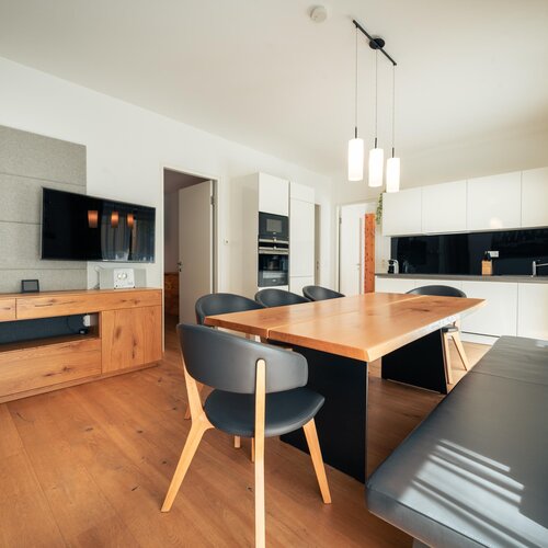 Open-concept living area with wooden dining table and white kitchen | © TIEBER