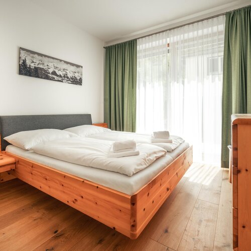 Wooden platform bed with white bedding in bright room | © TIEBER