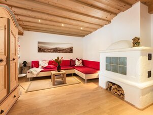 Gemütliches Wohnzimmer mit rotem Ecksofa und weißem Holzofen