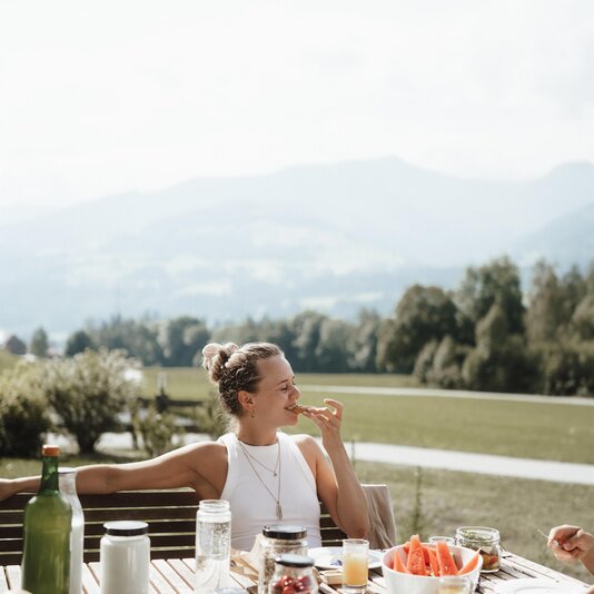 Woman sits at outdoor wooden table enjoying breakfast