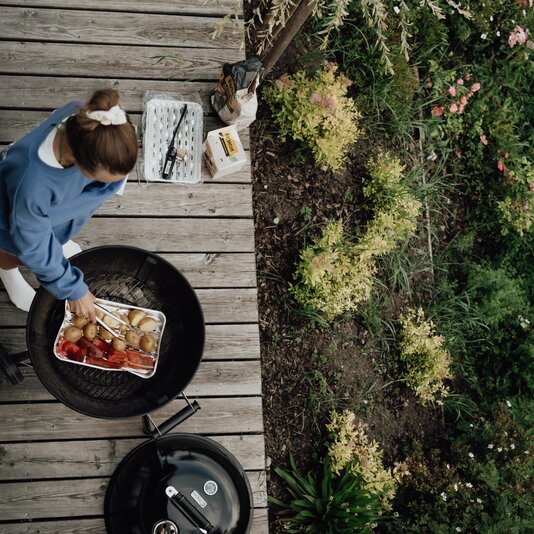 Person grilling vegetables on a round charcoal grill outdoors