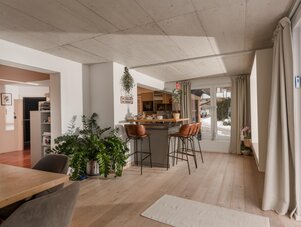 Bright modern open-plan kitchen and dining area with bar stools and plants