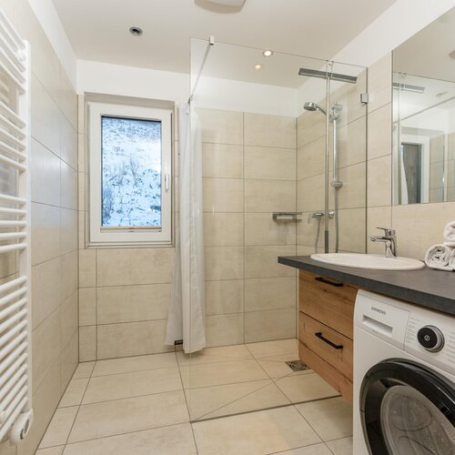 Modern beige-tiled bathroom with shower, sink, washing machine