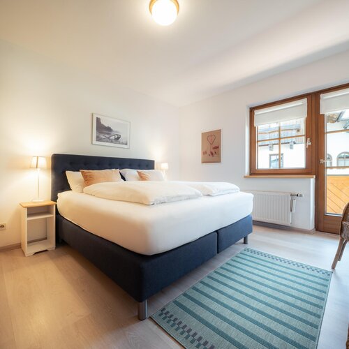 Bright bedroom with king bed, blue upholstered headboard, and balcony doors | © TIEBER