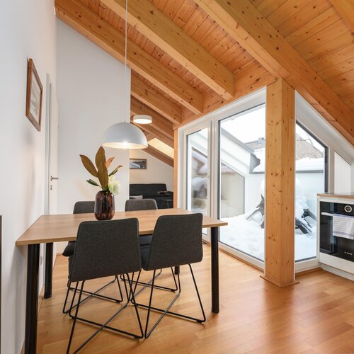 Dining area with wooden beams, large windows, and a vase