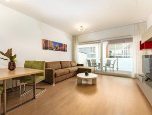 Spacious living room with brown sofa, green chairs, balcony access