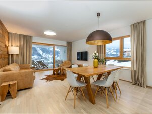 Living and dining area with wooden accent wall and snow outside.