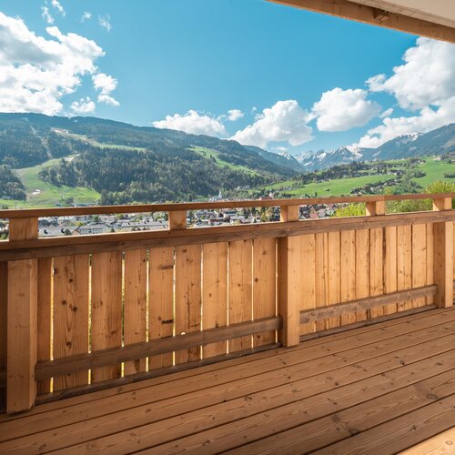 Wooden balcony railing overlooking a green valley and mountains