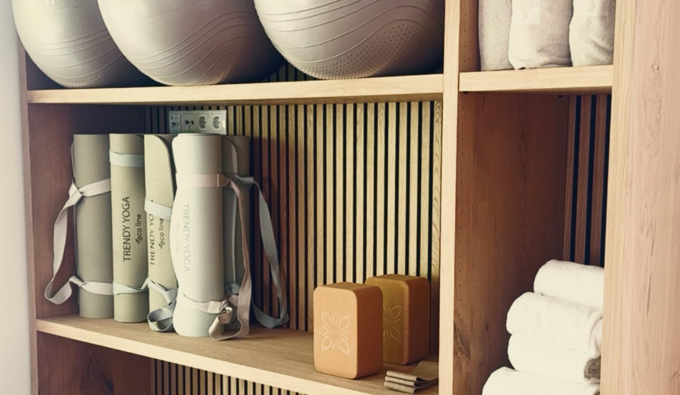 Wooden gym shelving with balls, mats and towels.