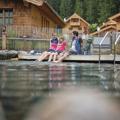 Familie zu dritt sitzt auf einem Holzsteg am See | © RAPHAELGABAUER.COM