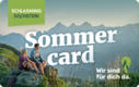 Two hikers sit on a rock with Sommer card text in mountains.